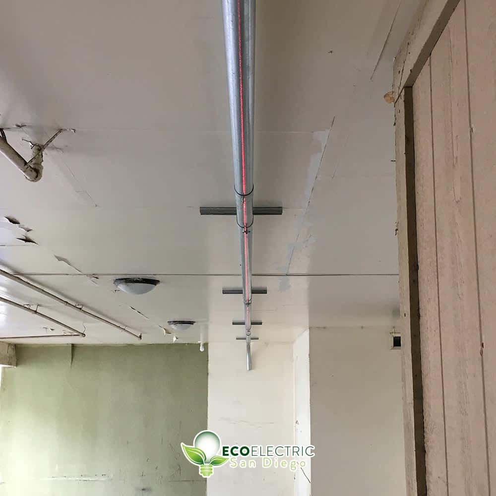 Electrical wiring in a metal pipe runs along a ceiling